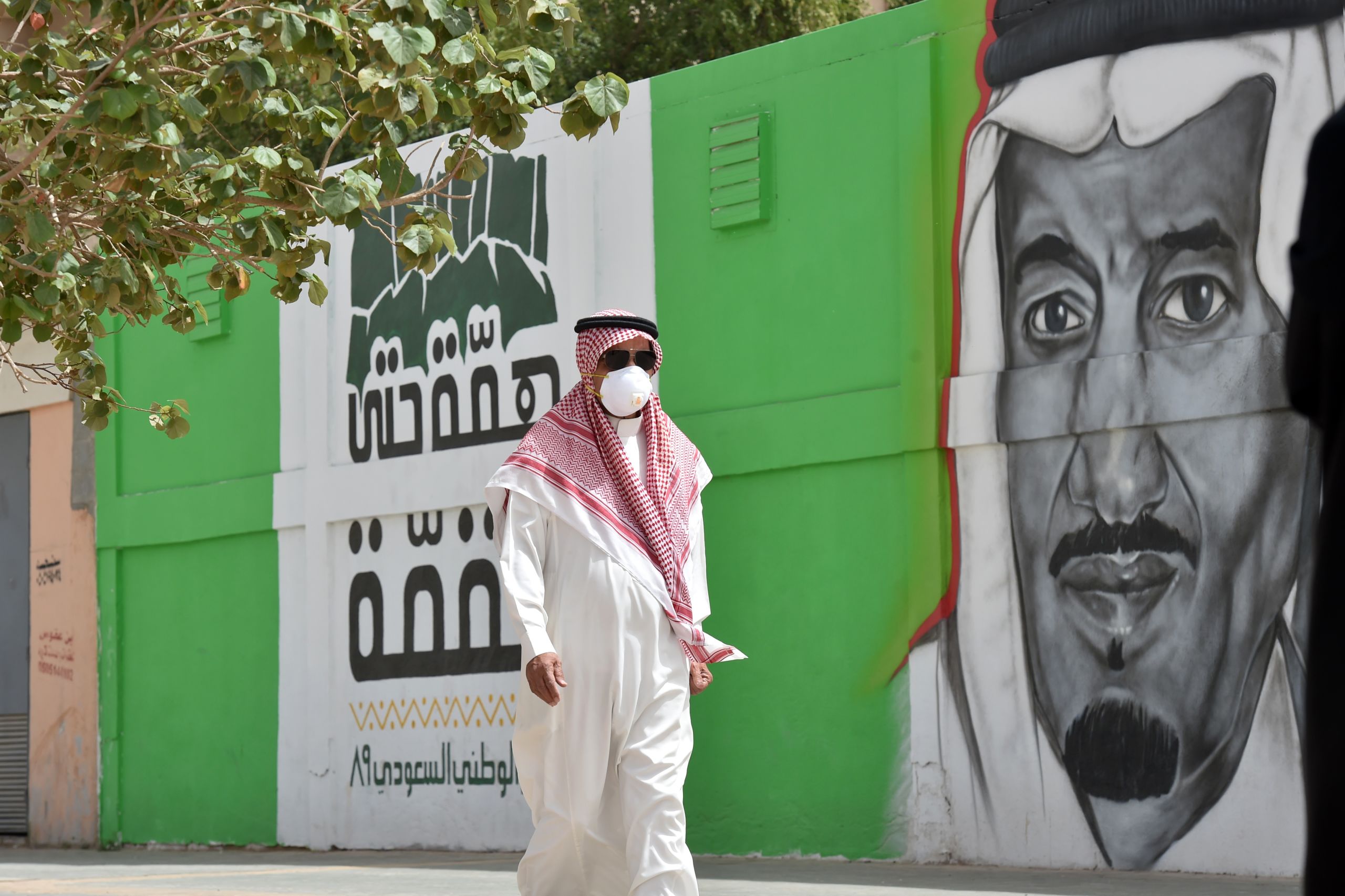Un Saoudien, portant un masque pour se protéger du coronavirus, passe à côté d’une fresque à l’effigie du Roi Salman, à Riyad le 15 mars. (AFP)
