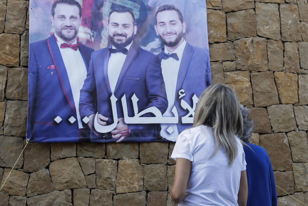 Des femmes libanaises regardent une affiche portant les photos de trois pompiers portés disparus, qui sont partis ensemble dans un camion de pompiers pour éteindre un incendie au port qui aurait déclenché l'énorme explosion du 4 août à Beyrouth, et qui ne sont jamais rentrés chez eux, avec la légende ci-dessous écrite en arabe "Les Héros." (AFP)