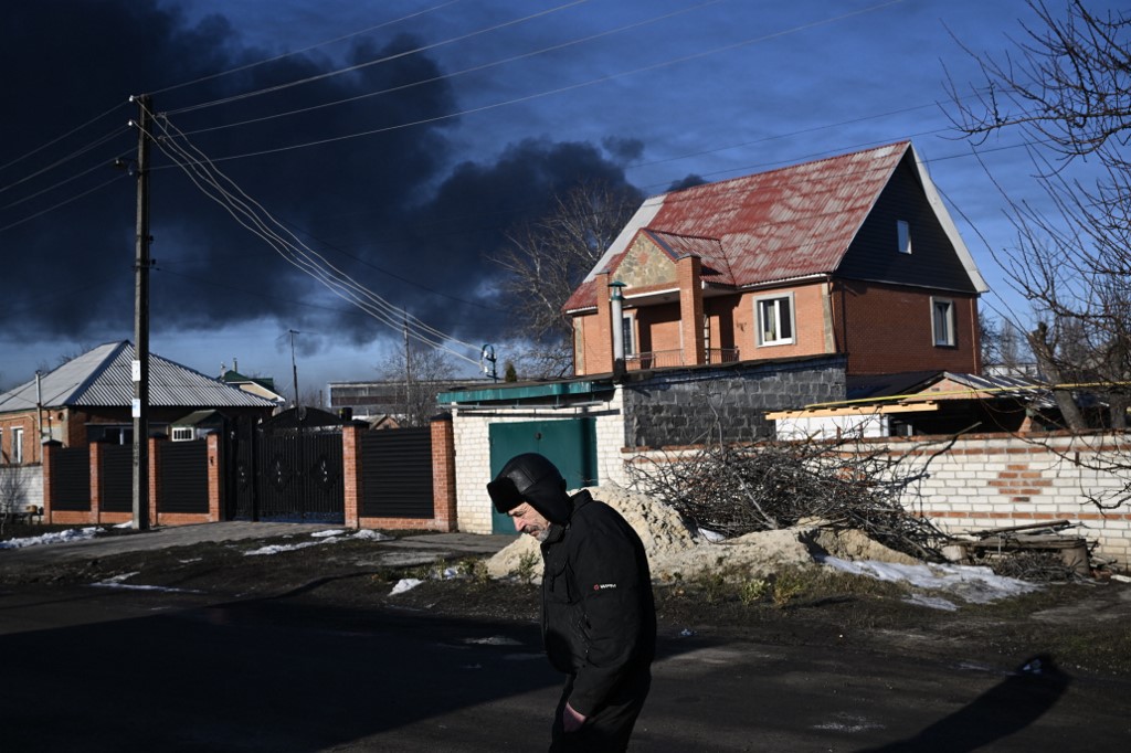Un homme marche dans une rue alors que de la fumée noire s'élève d'un aéroport militaire à Chuguyev près de Kharkiv, le 24 février 2022. (Photo, AFP)