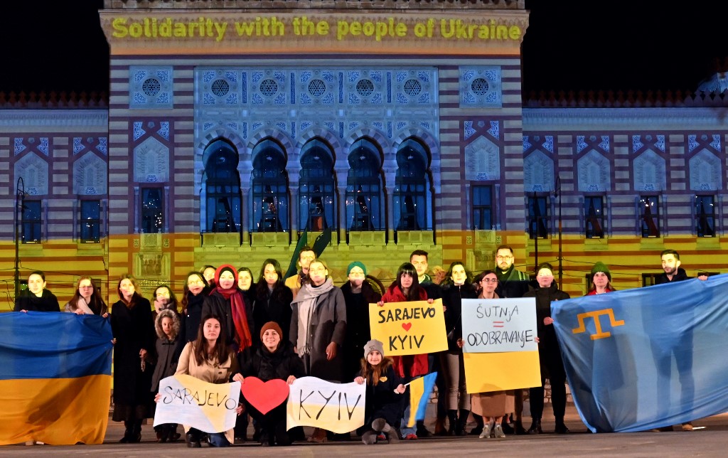 Des citoyens se rassemblent devant l'hôtel de ville de Sarajevo illuminé aux couleurs du drapeau ukrainien, le 24 février 2022 en fin de journée. (Photo, AFP)