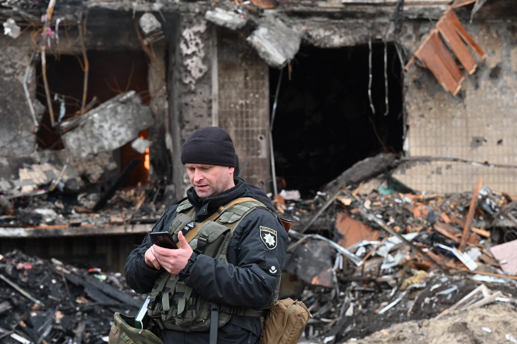 Un policier monte la garde devant un immeuble résidentiel endommagé de la rue Koshytsa, une banlieue de la capitale ukrainienne Kiev, où un obus militaire aurait frappé, le 25 février 2022. (Photo, AFP)