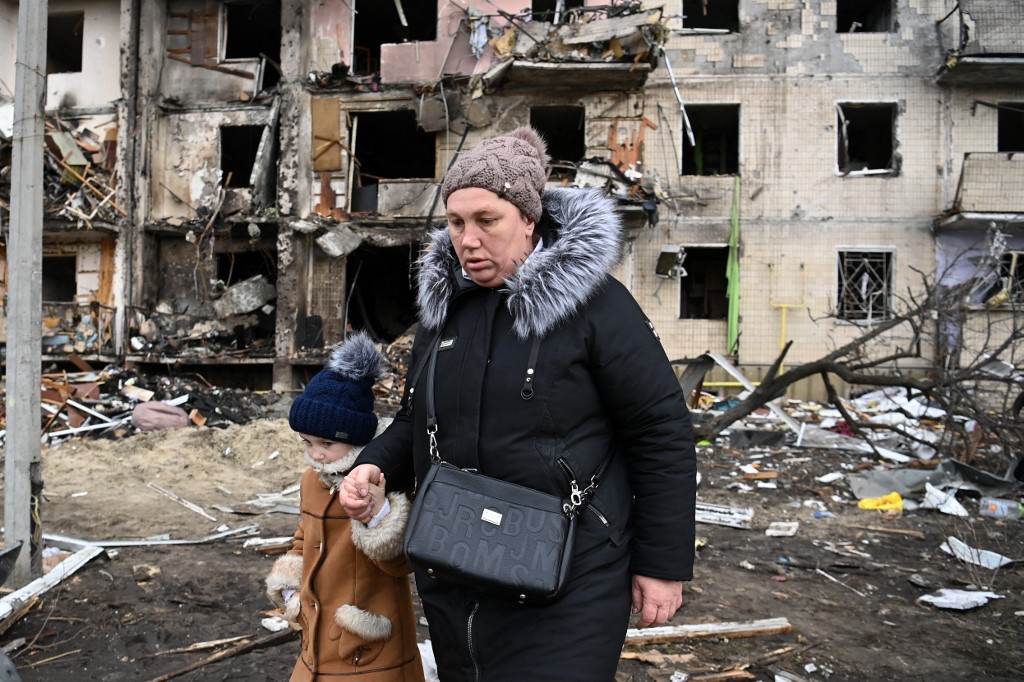 Une femme avec un enfant marche devant un immeuble résidentiel endommagé dans la rue Koshytsa, une banlieue de la capitale ukrainienne Kiev, où un obus militaire aurait été touché, le 25 février 2022. (Photo, AFP)