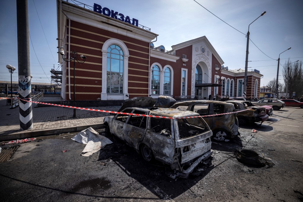 Une police ukrainienne se tient à côté de voitures calcinées devant une gare de Kramatorsk, dans l'est de l'Ukraine, qui était utilisée pour les évacuations civiles, après avoir été touchée par une attaque à la roquette tuant au moins 35 personnes, le 8 avril 2022 (Photo, AFP). 