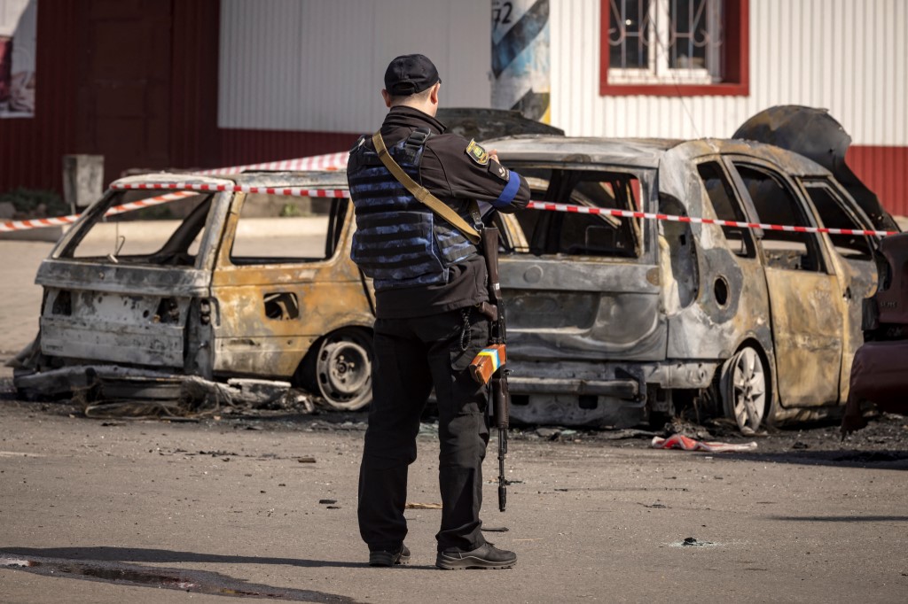 Une police ukrainienne se tient à côté de voitures calcinées devant une gare de Kramatorsk, dans l'est de l'Ukraine, qui était utilisée pour les évacuations civiles, après avoir été touchée par une attaque à la roquette tuant au moins 35 personnes, le 8 avril 2022 (Photo, AFP). 