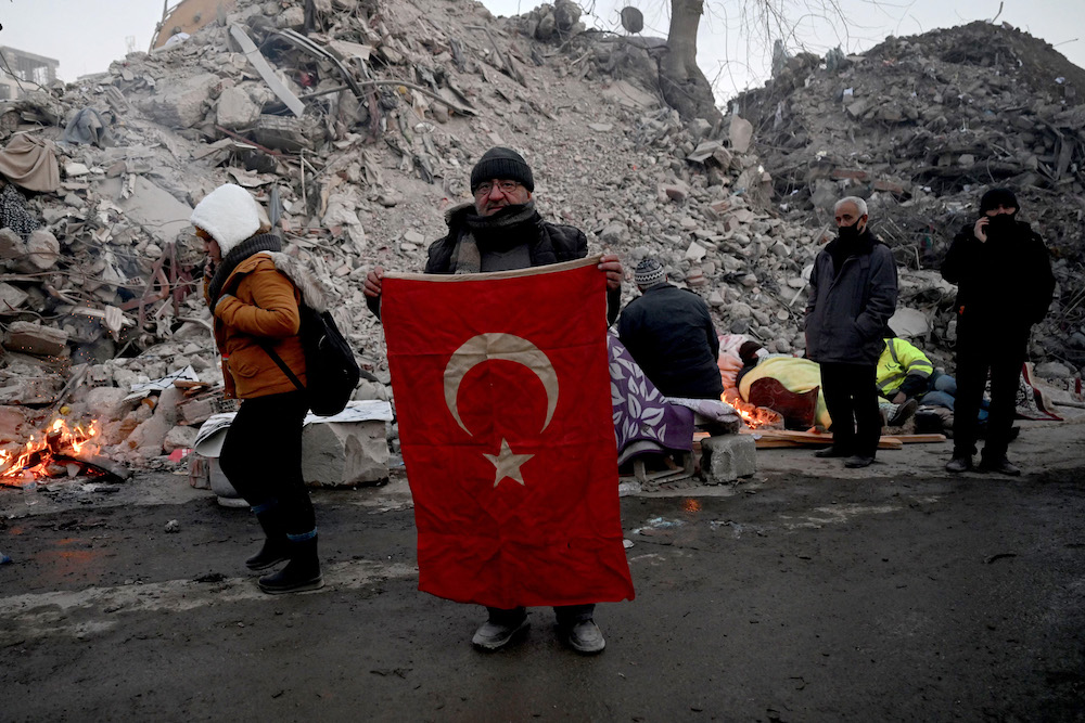 Un membre de la famille d’une victime brandit le drapeau national devant les décombres de bâtiments effondrés, alors que les équipes de secours recherchent des victimes et des survivants, à Kahramanmaras, le 12 février 2023. (AFP)