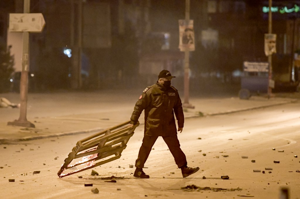 Un membre de la Garde nationale tunisienne traîne un treillis en bois en feu lors d'affrontements avec des manifestants dans la banlieue d'Ettadhamen, dans la banlieue nord-ouest de la capitale tunisienne, Tunis, le 17 janvier 2021. (AFP)