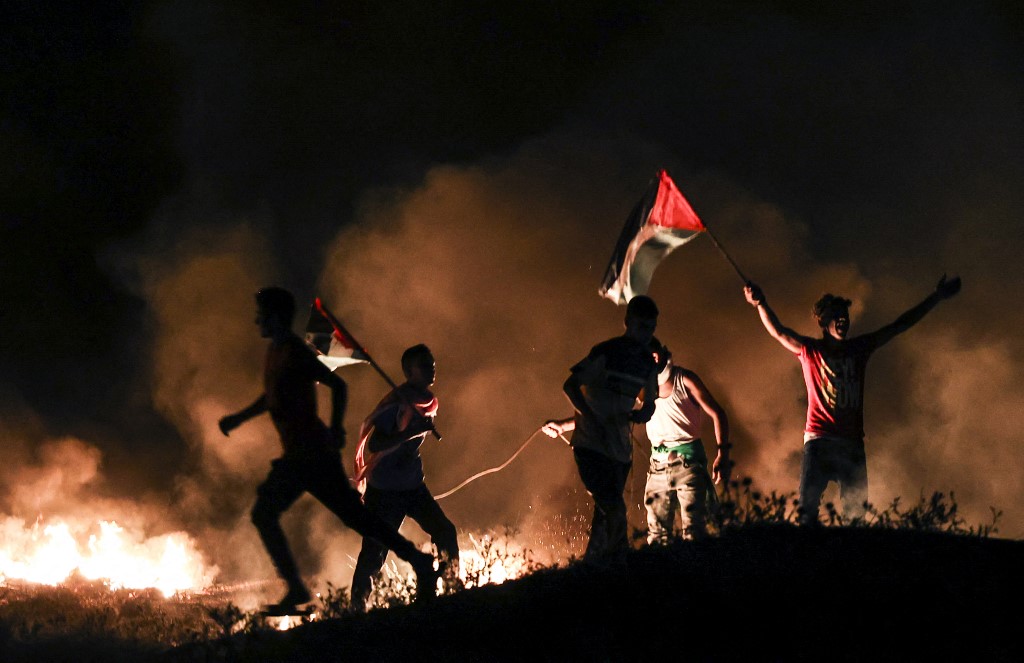 Des manifestants palestiniens lèvent des drapeaux nationaux alors qu'ils brûlent des pneus lors d'une manifestation à l'est de la ville de Gaza, à la frontière avec Israël. (AFP)