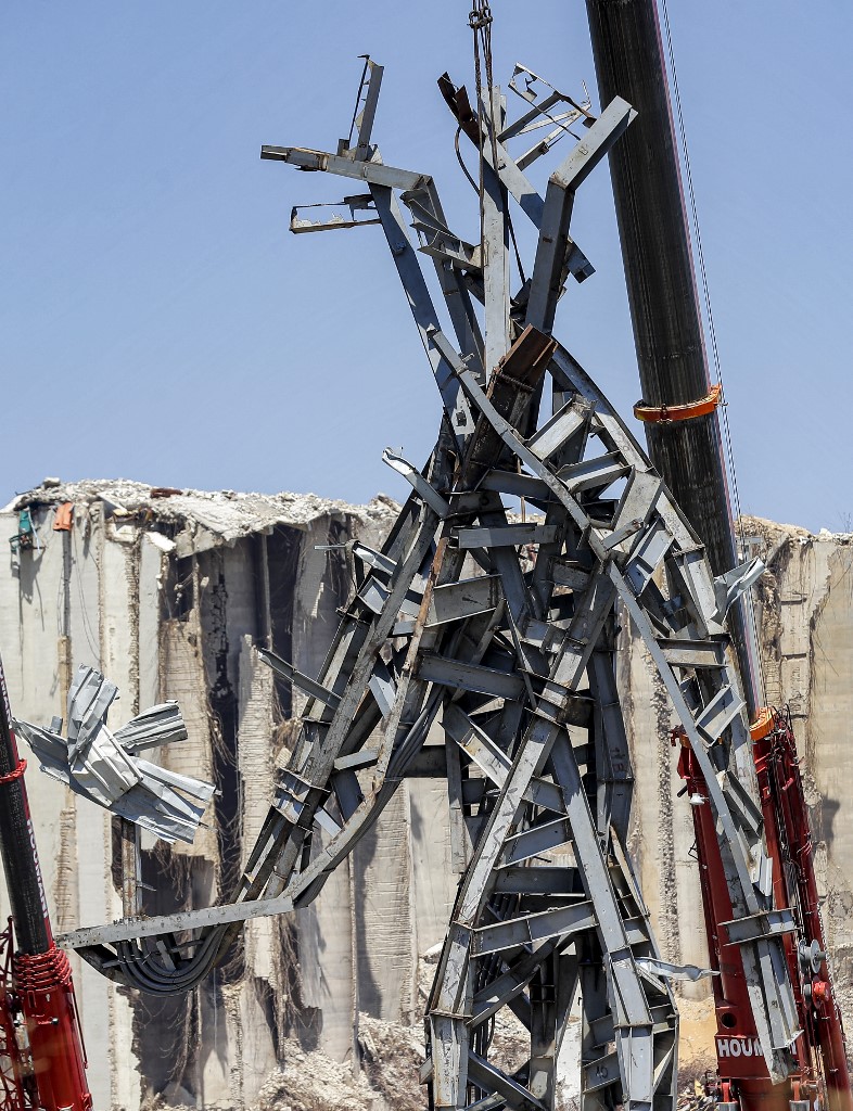 Cette photo prise le 28 juillet 2021 montre une vue d'une sculpture en acier de 25 mètres de haut surnommée "Le geste" par l'artiste libanais Nadim Karam, fabriquée à partir de débris résultant de l'explosion dans le port de la capitale libanaise Beyrouth qui a pris lieu le 4 août 2020, suspendu à une grue sur le site de l'explosion au port près du désormais emblématique silo à grains endommagé