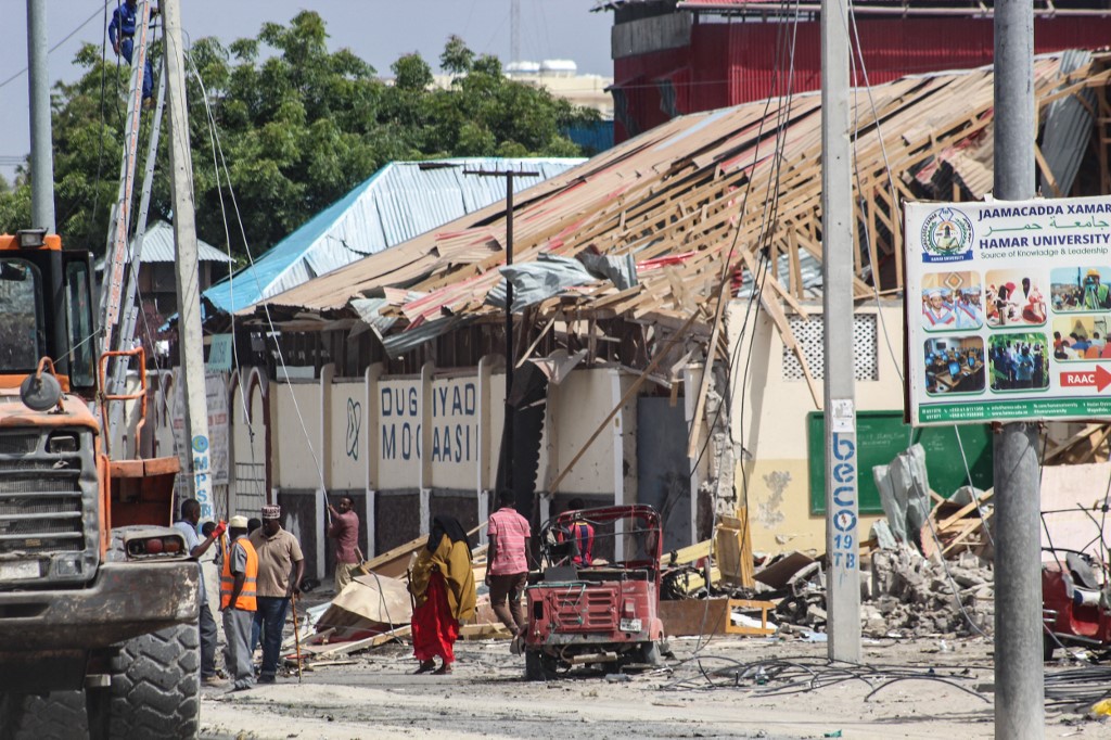 People walk past bomb explosion site in Mogadishu, Somalia, on November 25, 2021. Five people were killed and over a dozen injured in a car bombing near a school in Somalia's capital Mogadishu on November 25, 2021, a security official said, in the latest attack to hit the troubled country