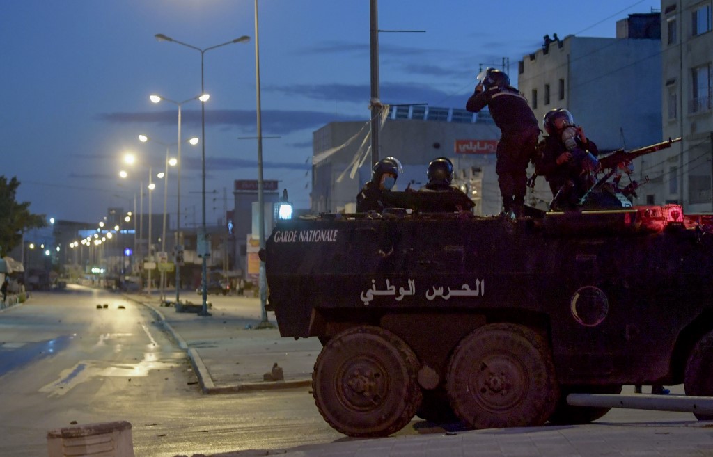 Des membres de la Garde nationale tunisienne sont assis au sommet de leur véhicule blindé, stationné dans une rue au milieu d'affrontements avec des manifestants à la suite d'une manifestation dans le quartier d'Ettadhamen dans la capitale Tunis, le 17 janvier 2021. (AFP)