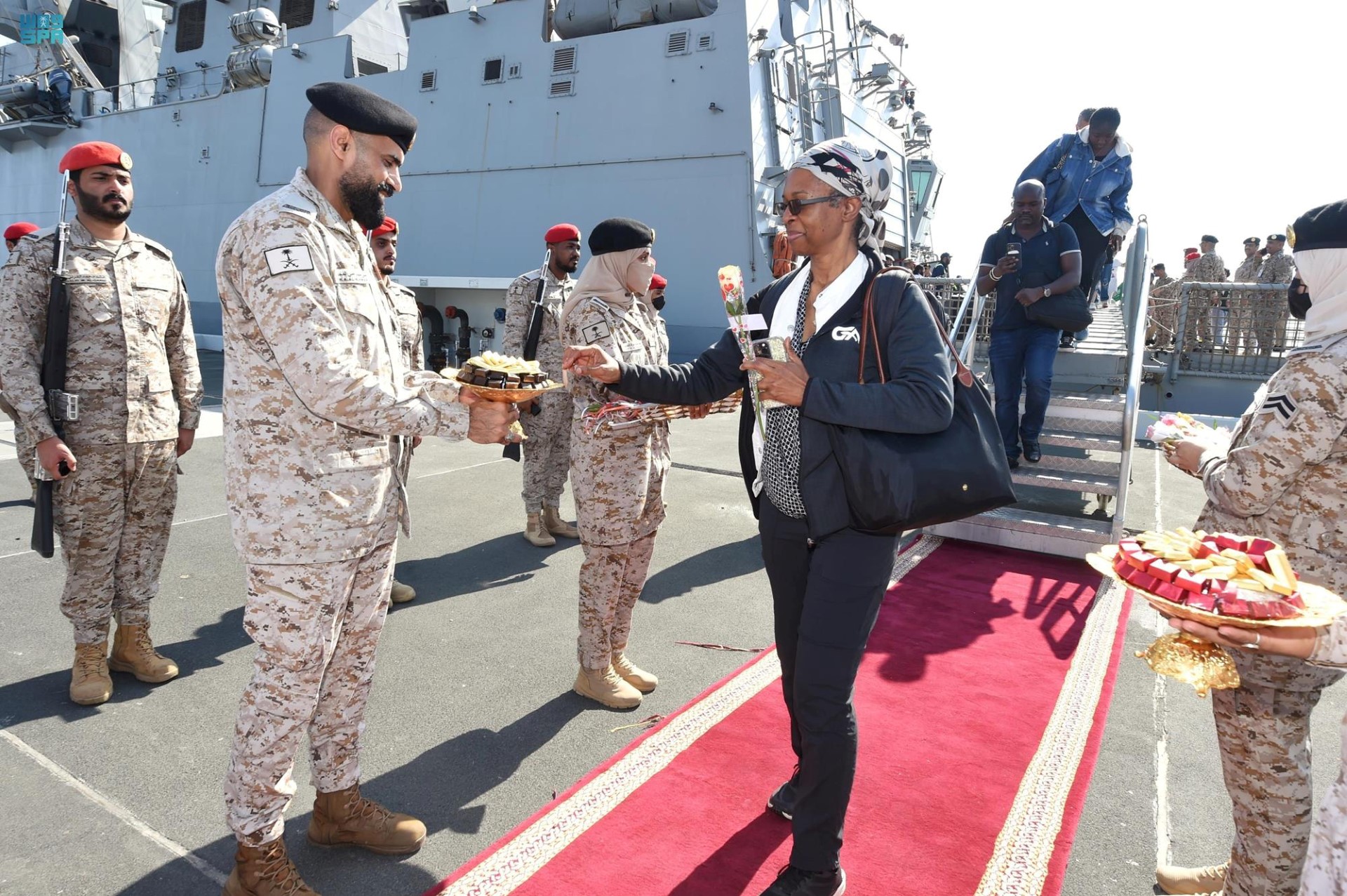 Une photo fournie par l'agence de presse saoudienne (SPA) le 22 avril 2023 montre des membres des forces armées distribuant des chocolats et des fleurs aux citoyens saoudiens et à d'autres ressortissants à leur arrivée à Djeddah, après leur sauvetage du Soudan. Un navire transportant des citoyens saoudiens et d'autres ressortissants sauvés du Soudan meurtri par les combats est arrivé à Djeddah, a indiqué la télévision saoudienne, lors de la première évacuation annoncée de civils depuis le début des combats. (Photo par SPA/AFP)