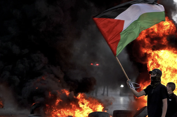 Un manifestant masqué agite un drapeau palestinien près d’un pneu en feu lors d’affrontements avec les forces israéliennes, à la suite d’une manifestation pour dénoncer la marche nationaliste annuelle des drapeaux à travers Jérusalem. (AFP)