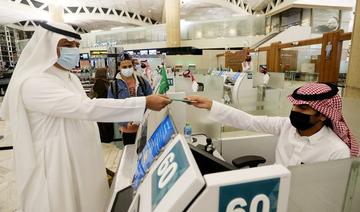 Un Saoudien portant un masque récupère son passeport auprès d'un agent de l'immigration à l'aéroport international Roi Khaled à Riyad, en Arabie Saoudite. (REUTERS)