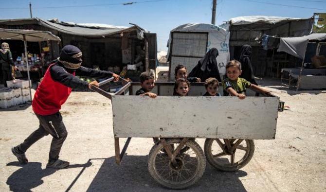 Un jeune homme pousse une charrette avec des enfants assis à l'intérieur du camp kurde d'al-Hol, qui abrite des proches de combattants présumés du groupe État islamique (EI), dans le gouvernorat de Hasakeh, dans le nord-est de la Syrie, le 23 juin 2021. (Delil Souleiman /AFP)