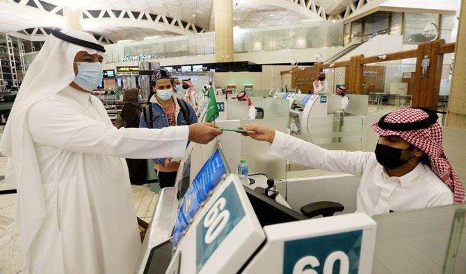 Un Saoudien portant un masque récupère son passeport auprès d'un agent de l'immigration à l'aéroport international Roi Khaled à Riyad, en Arabie Saoudite. (REUTERS)