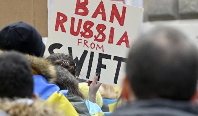 Un manifestant tient une affiche indiquant «Bannir la Russie de SWIFT» lors d'une manifestation contre l'invasion de l'Ukraine par la Russie, le 26 février 2022 devant l'ambassade de Russie à Vienne, en Autriche. (Photo, AFP)