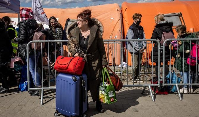 Une femme se tenant debout avec ses valises, tandis que des réfugiés ukrainiens attendent un bus après avoir traversé la frontière ukraino-polonaise au poste frontière de Medyka, en Pologne. (Fichier/AFP) 