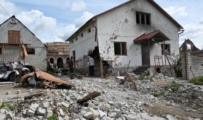 Des résidents locaux se tiennent à côté d'une maison fortement endommagée dans le village de Mala Rogan, à l'est de Kharkiv, le 15 mai 2022. (Photo, AFP)