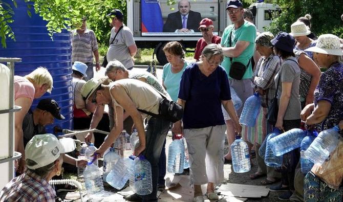 Les résidents locaux obtiennent de l'eau alors que le Premier ministre russe Mikhail Mishustin apparaît sur un écran à Marioupol le 3 juin, le 100e jour de l'invasion russe de l'Ukraine. (Photo, AFP)