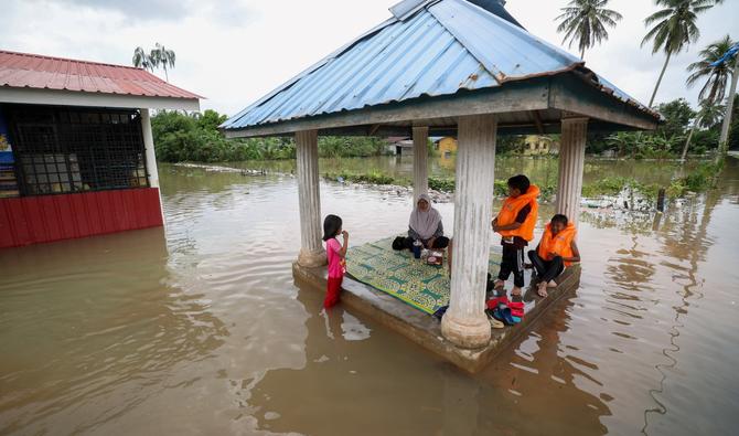Une famille est assise dans une pergola entourée par les eaux de crue à Pasir Mas, dans l'État de Kelantan, dans le nord de la Malaisie, le 21 décembre 2022. (Photo, AFP)