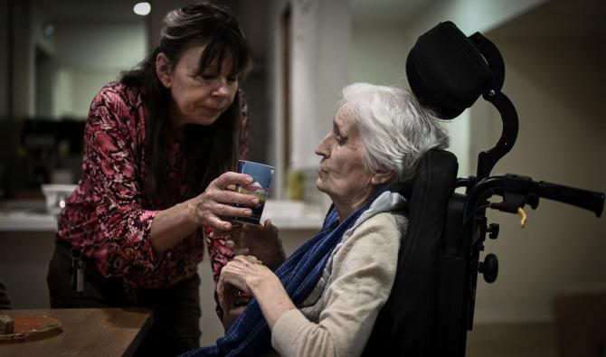 Un personnel soignant (G) aide un patient atteint de la maladie d'Alzheimer à l'heure du déjeuner dans l'un des lieux de vie du village Landais Alzheimer à Dax, dans le sud-ouest de la France, le 30 novembre 2023. 